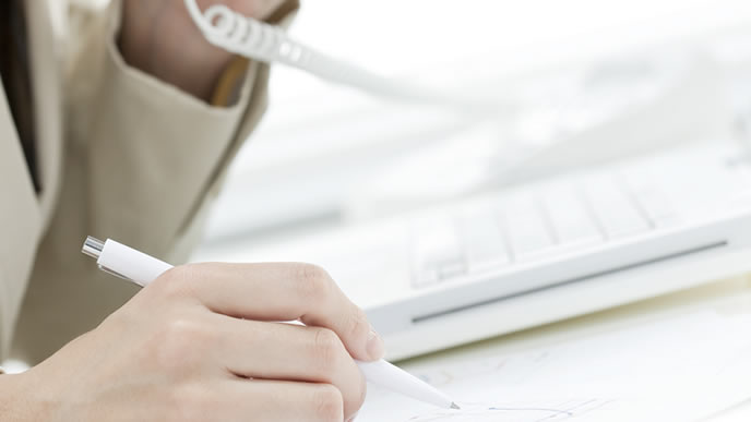 電話相手の情報をメモに取る女性社員