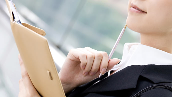 スケジュールを手帳に書き込むOL