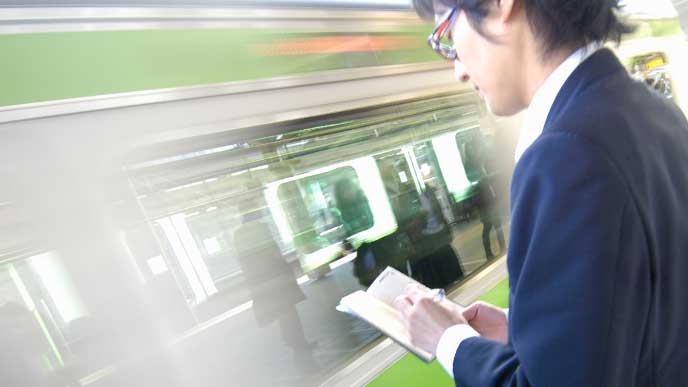 ホームで電車を待ちながら本を読んでる男性