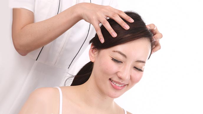 女性の頭皮をマッサージするエステティシャン