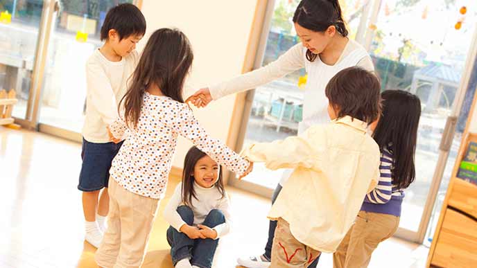 子供たちと円になって手を繋ぐ保育士