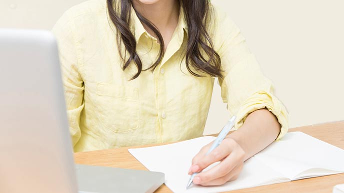 パソコンを見ながらノートをチェックする保育士