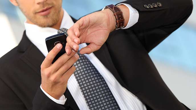スマホと腕時計を一緒に見るビジネスマン