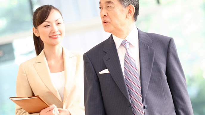 社長の後ろで笑顔で答える女性秘書