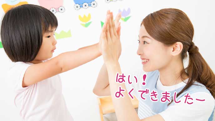子供をハイタッチして褒める幼稚園教諭