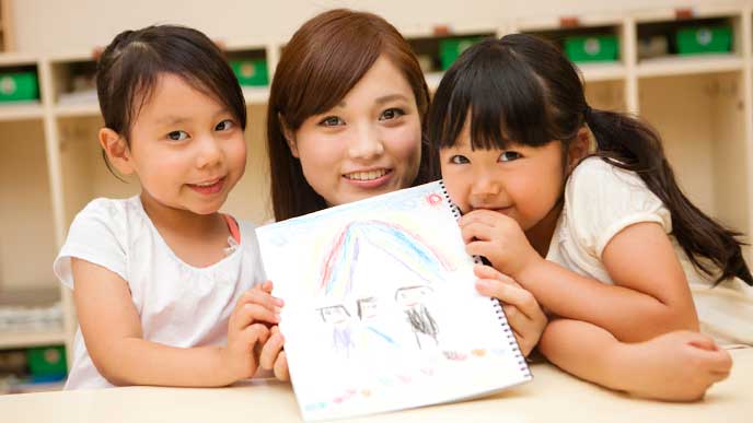 子供と一緒にクレヨンで描いた絵を見せる幼稚園教諭