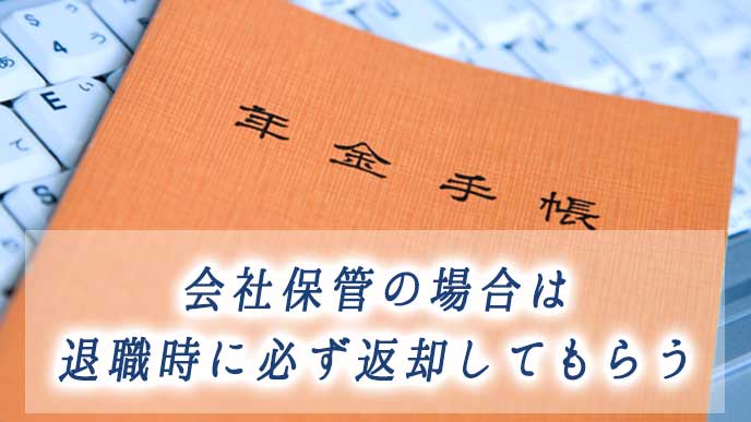 会社のノートパソコンの上に置かれた年金手帳