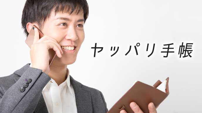 手帳でスケジュールを見ながら営業先と電話をしているビジネスマン