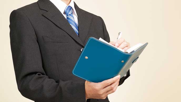 仕事のスケジュールを手帳に書くビジネスマン