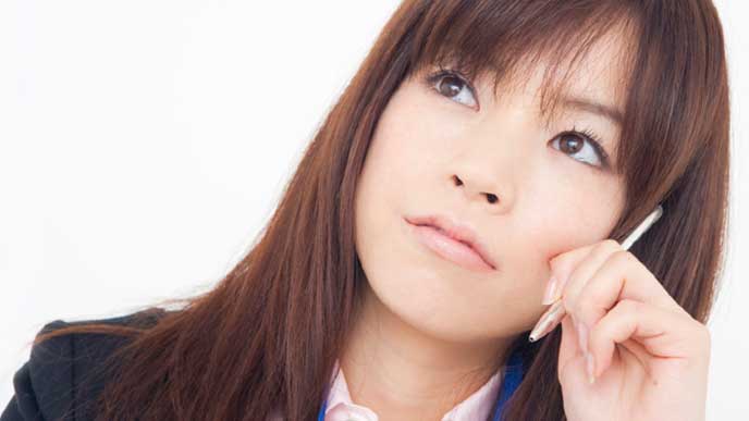 ペンを持って考え込んでいるOL