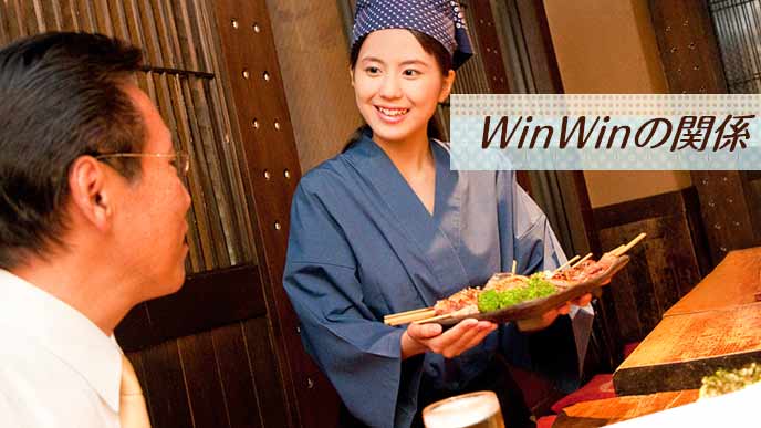 居酒屋で料理を持ってくる店員とお客の笑顔のやりとり