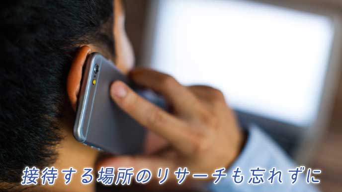 パソコンで調べものをしてスマホで電話をするビジネスマン