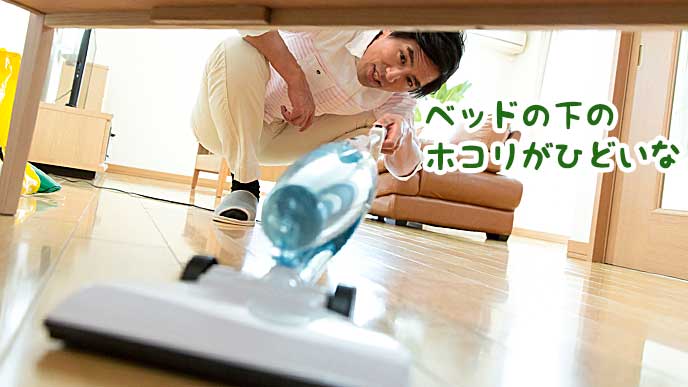 ベッドの下に掃除機をかける男性