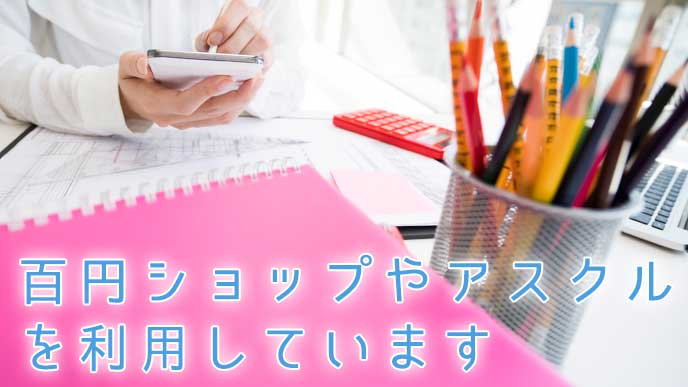 ペン立てとピンクのファイルが置かれたデスクで仕事をしている会社員の女性