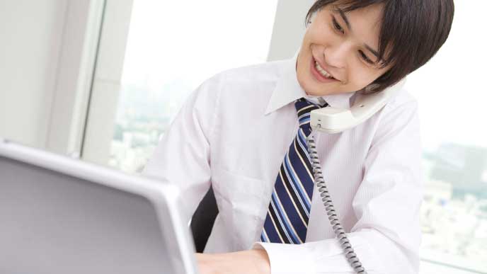 取引先と電話をしながらパソコンを使い仕事をしているビジネスマン