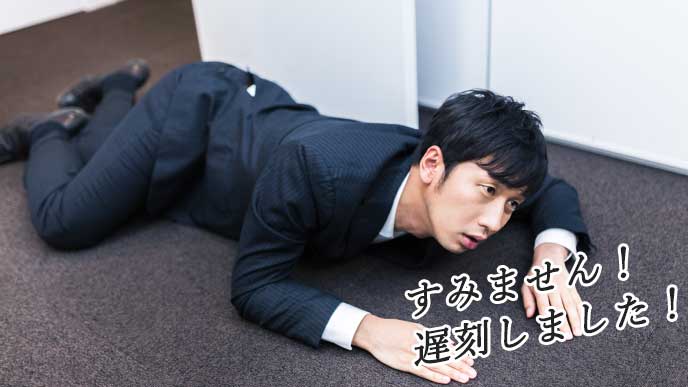 遅刻をしてオフィスでうつ伏せになりながら謝るサラリーマン