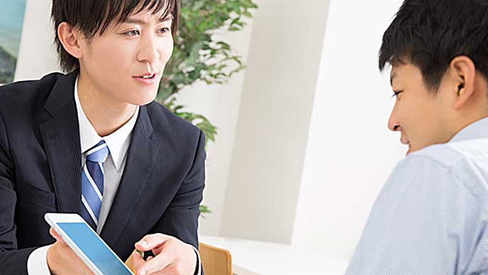取引先の相手にタブレットPCの画面を見せているビジネスマン
