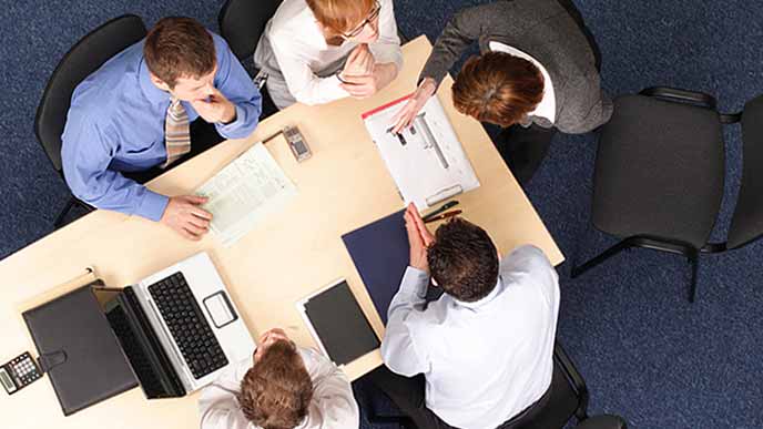 机を囲んで打ち合わせする社員