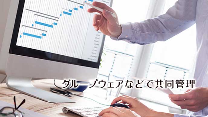 パソコン画面の進行表をチェックする社員