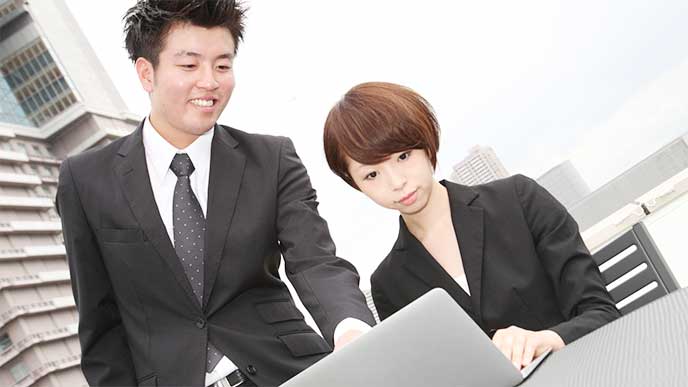 パソコンを見ながら女性と話してる男性社内SE