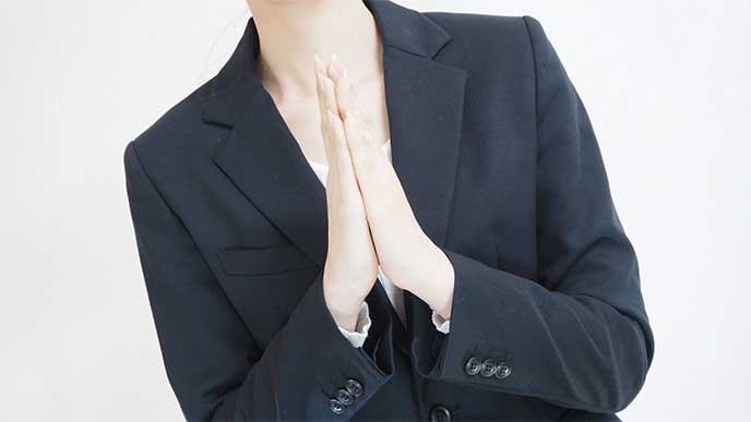 手のひらを合わせ態度で謝罪を示す女性社員