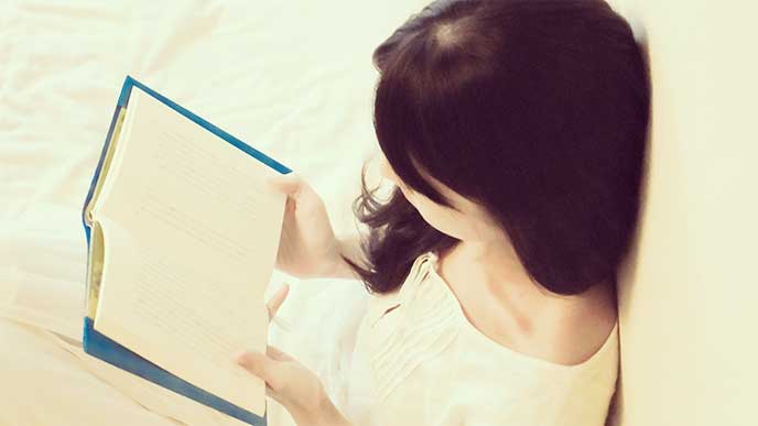 壁にもたれかかって本を読んでる女性