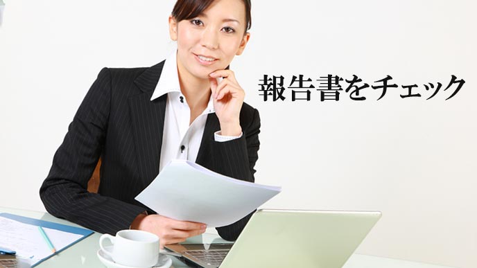 ラップトップのデータを見ながら書類をチェックする女性