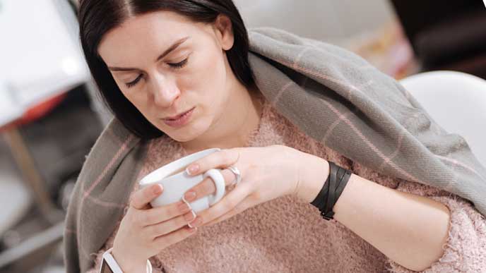 肩までブランケットをかけてコーヒーを飲む女性社員