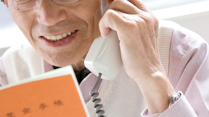 年金手帳を見ながら電話で問い合わせる年配の男性