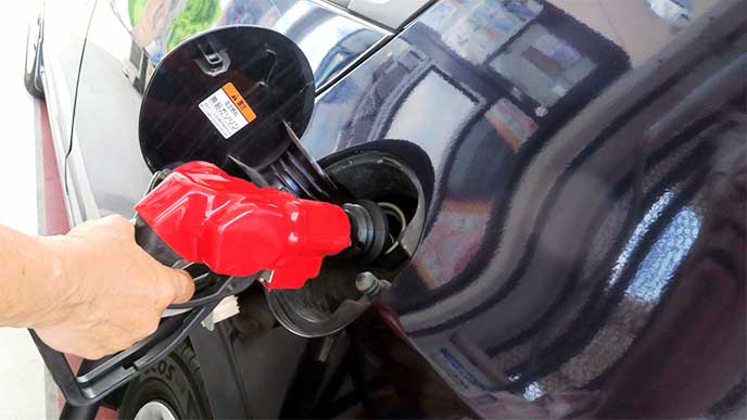 ガソリンスタンドで車に給油してる男性スタッフ