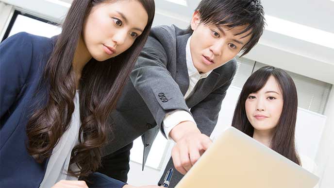 女性社員が使うパソコンを指差し指摘してる男性社員