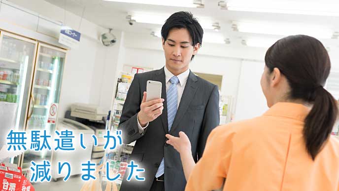 スマホアプリを見ながらコンビニで買い物を済ませる会社員