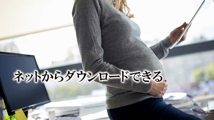 PCの傍で印刷した用紙を見る妊婦