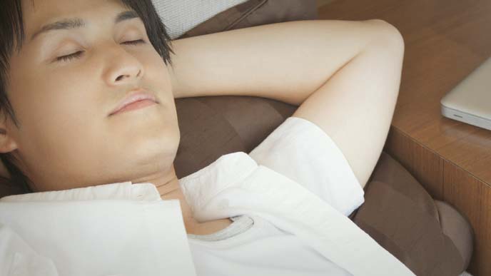 頭の後ろで手を組み、目を瞑り、ソファで寝転ぶ男性