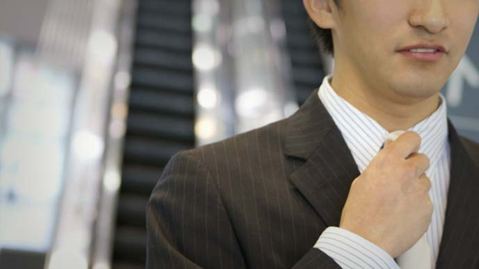 エスカレータをバックにネクタイを締め直す男性