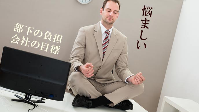 会社のデスクの上で座禅を組む中間管理職の男性