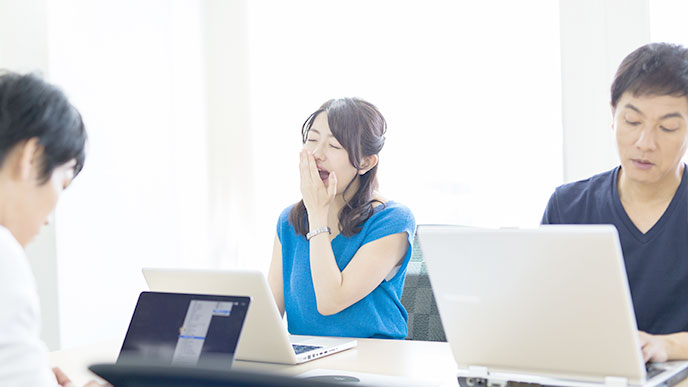 ノートパソコンの前にあくびをする女性社員