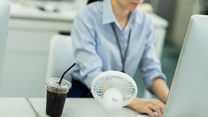 卓上扇風機をデスクに置く女性社員