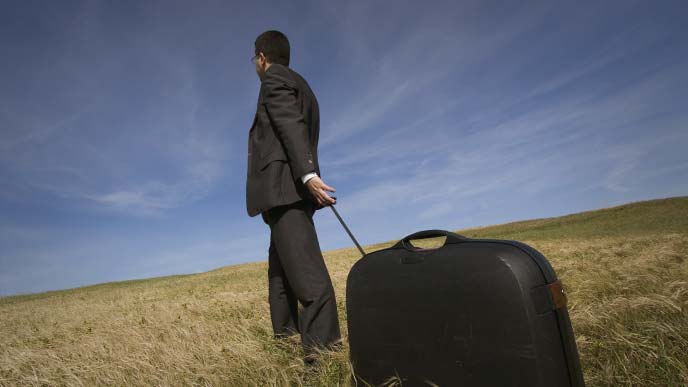 スーツケースを引きずりながら荒野を進むスーツ姿の男性