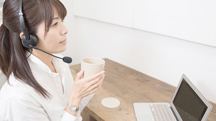 コーヒーを飲みながら働くヘッドセットを耳にかけた女性