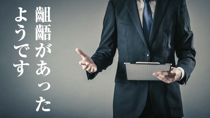 バインダーを手に淡々を齟齬を報告する男性