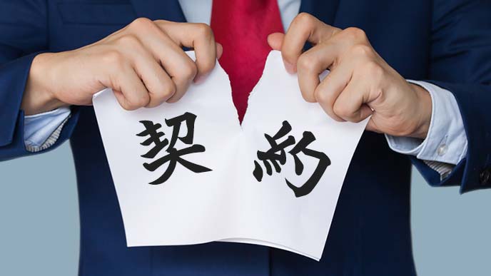 契約と書かれた紙を破くスーツ姿の男性