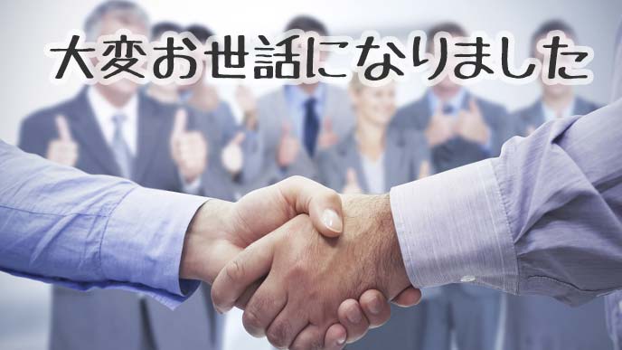 男性2人の握手とスタッフたち