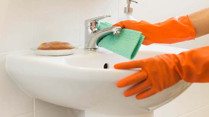 オレンジ色の手袋で洗面台を拭いている様子
