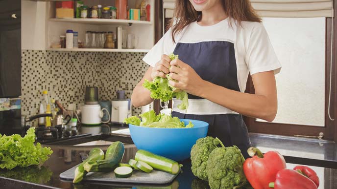 野菜をちぎってボウルに入れているエプロン姿の女性