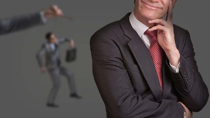 操り人形な男性をバックにダークにほくそ笑む男性