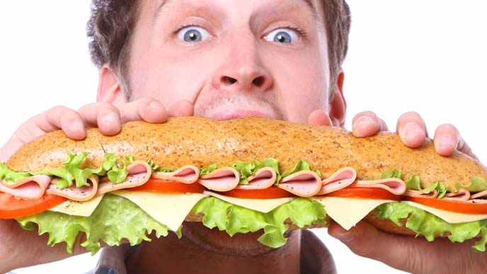 大きなサブマリンサンドに食らいつく男性