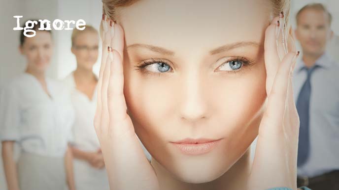 こめかみに手を添えながらそっと後ろを伺う女性と背後から話しかけてくる同僚たち