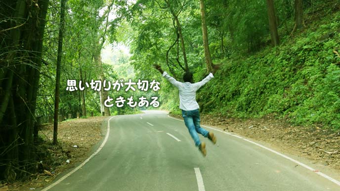 山の中の舗装道路でジャンプする人の後ろ姿