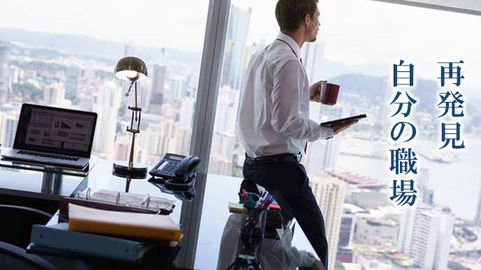 職場の高層ビルの窓から外を見つめるビジネスマン